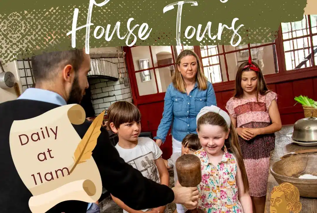 A group of children and an adult guide gather in a historical kitchen. A girl holds a wooden tool, while a scroll reads "Daily at 11am." The text above says "Children’s House Tours.